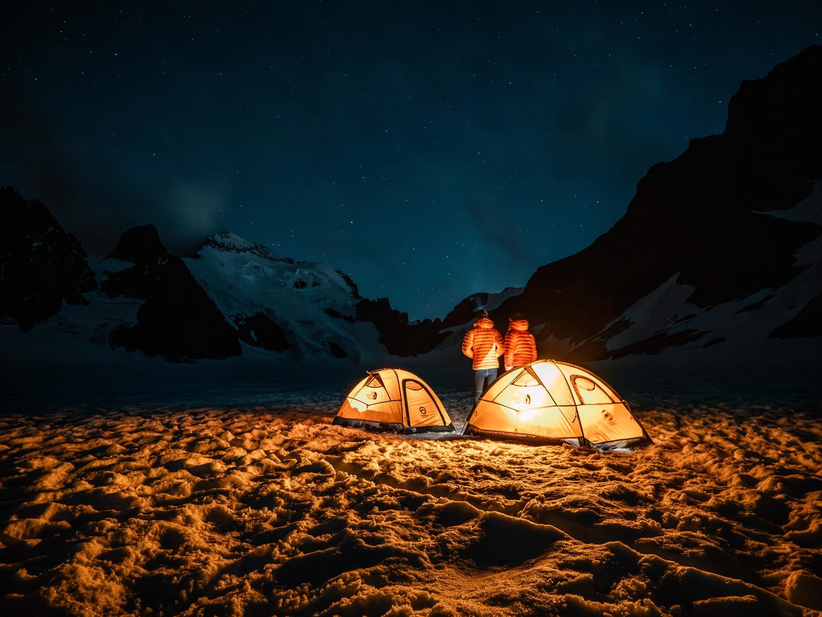 Two tents lit at night under the peaks