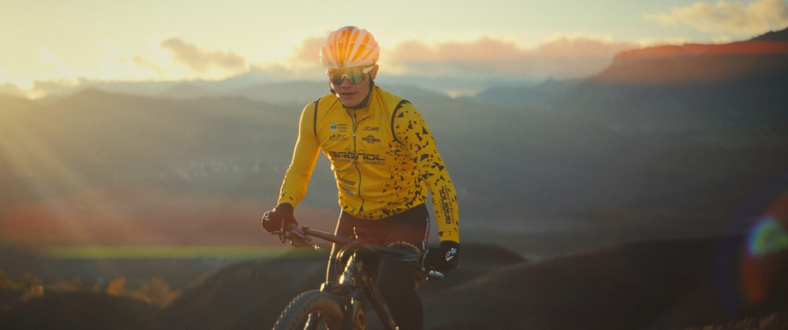 Malo riding a ridge at sunset in the yellow team jersey